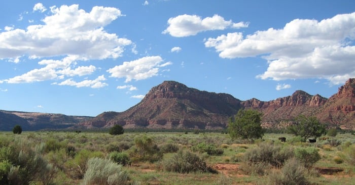 A daytime photo of Thunder Mountain Kaibab Paiute Indian Reservation with blue skies and white cloud above and a rolling landscape of green.