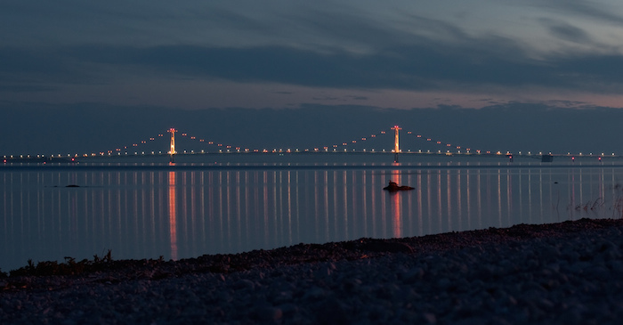 The Mackinac Bridge at twilight with colored lights that are reflecting in the water.