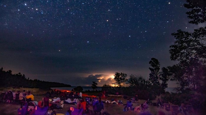 People sitting on the lawn lookin gup at a starry night sky at the Newport State Park during its Perseid meteor showers event.