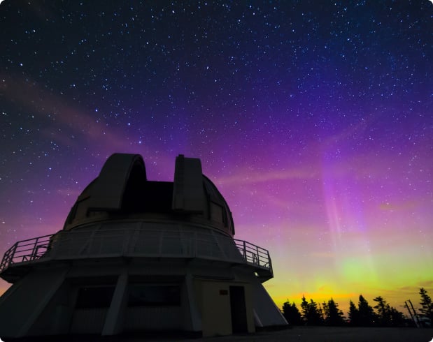 Vibrant colorful sunset with starry skies, and silhouette of an observatory dome in the foreground.