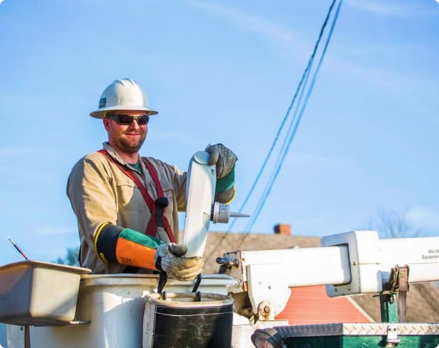 A workman in a hardhat, up high in a bucket truck, replaces a streetlight.