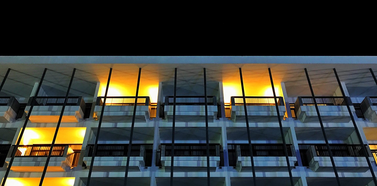 Apartment building with several balconies lit up at night, with no people on them.