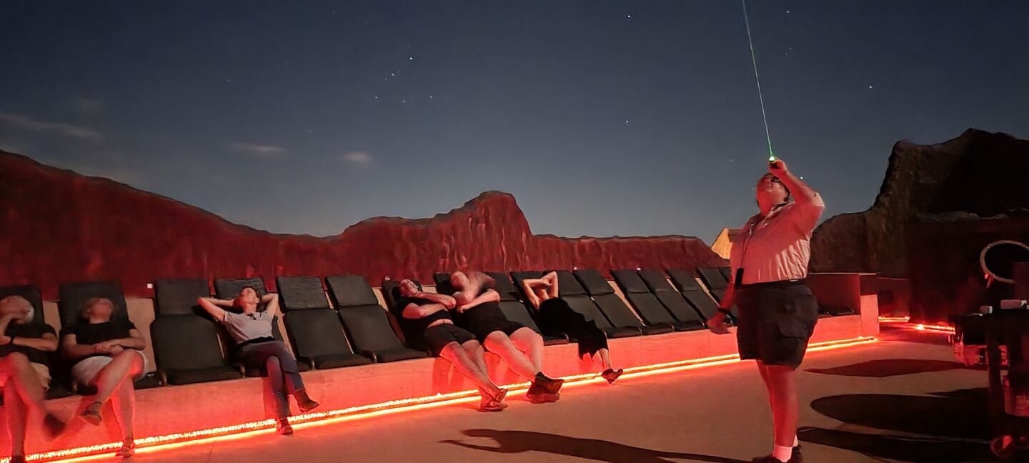 People look up at the stars while sitting a long a bench. 