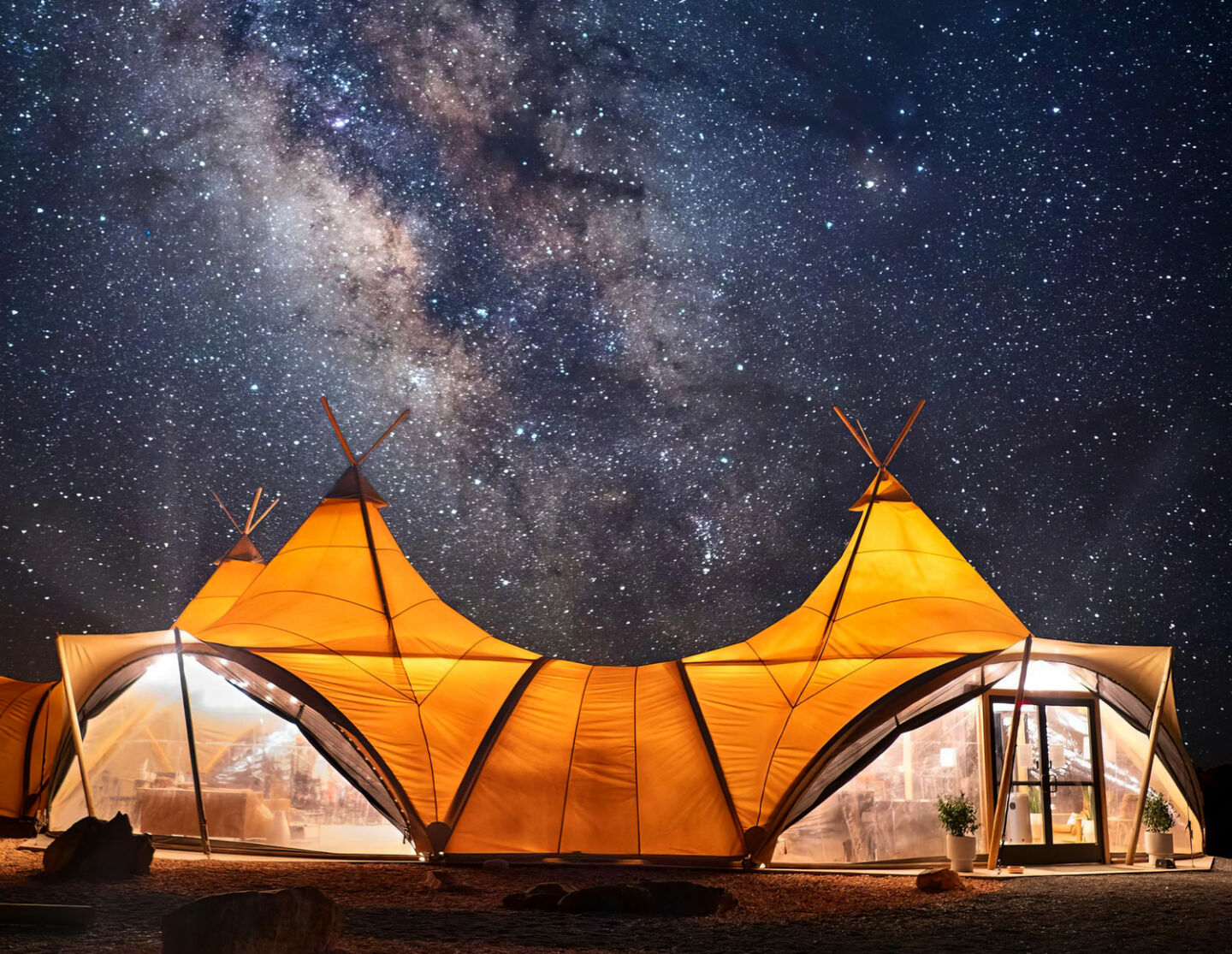 A tent cabin lit up at night, under a glorious Milky Way in the sky.