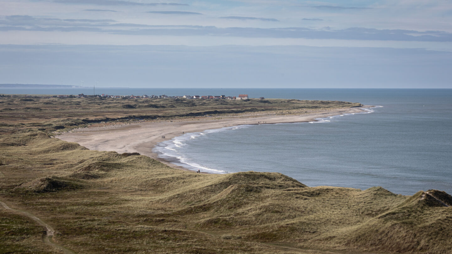A small coastal village in the distance with sand dunes in the foreground.