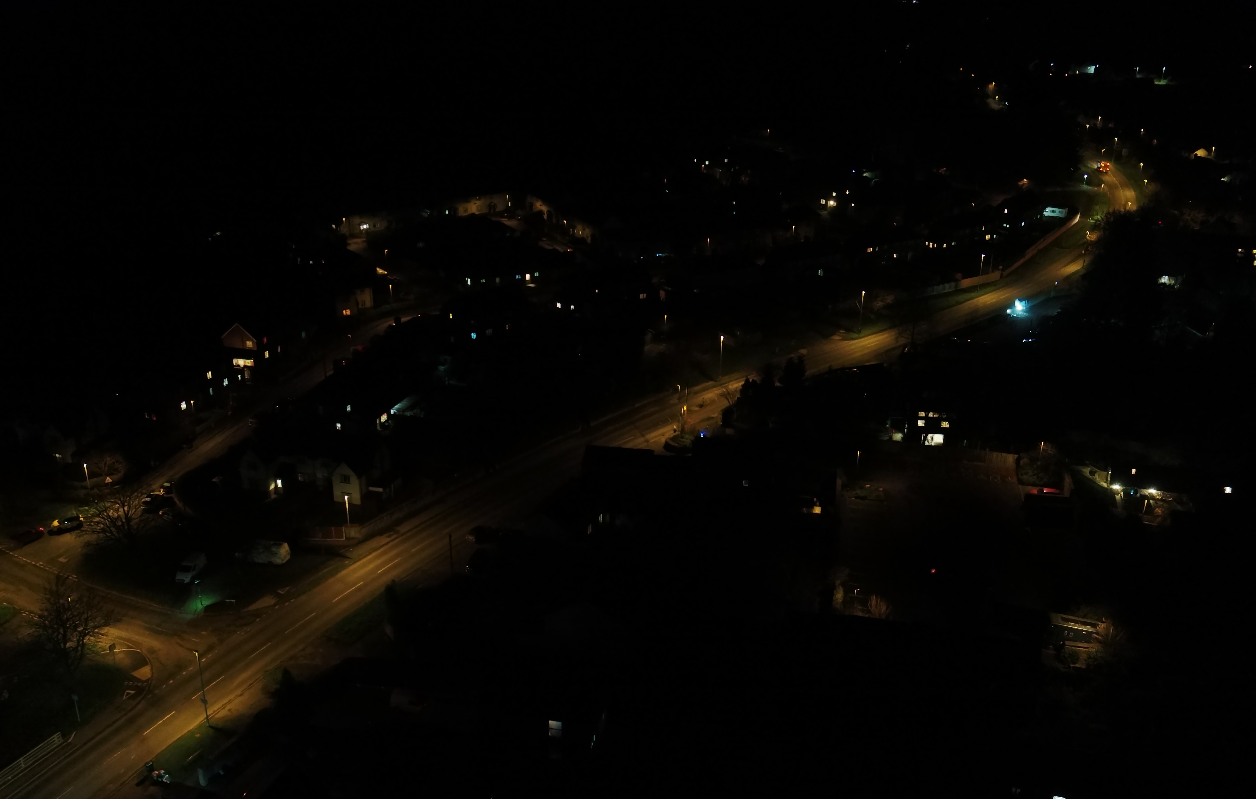 A drone aerial view of a street with dark sky friendly dim and warm lighting.