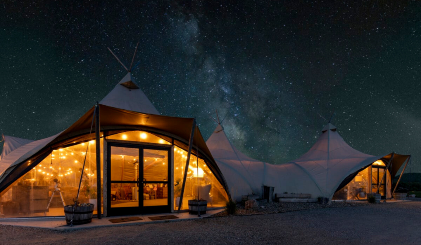 A large canvas canopy tent sits beneath a starry night sky.