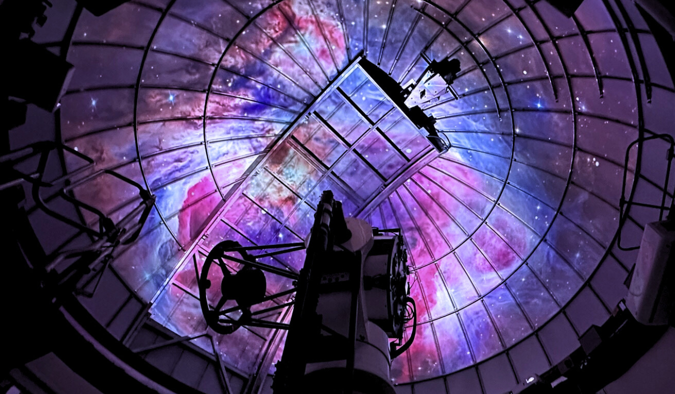 Colorful lights projected on a observatory ceiling above a telescope.