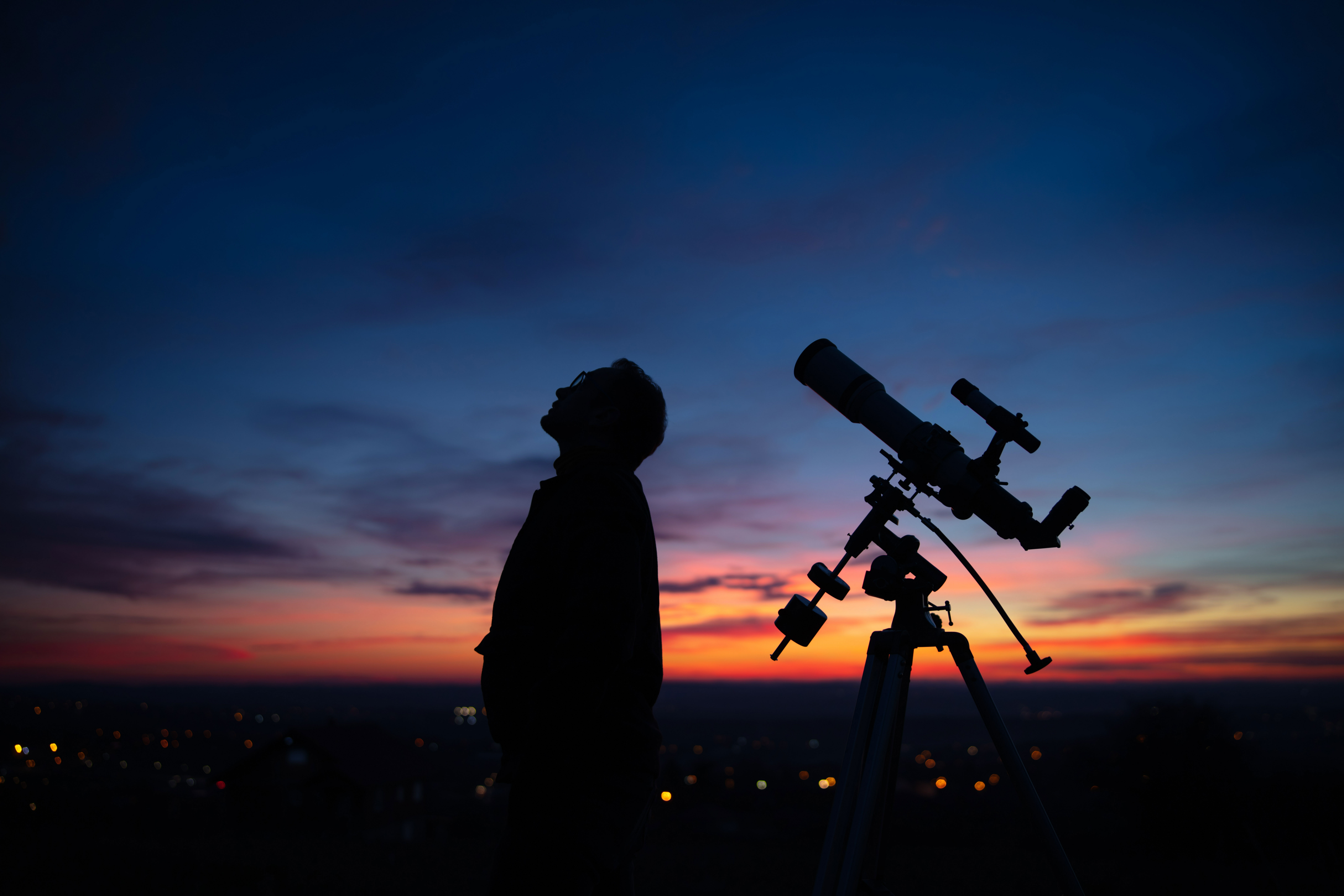 Stargazer looking at the sky at dusk beside a telescope. 