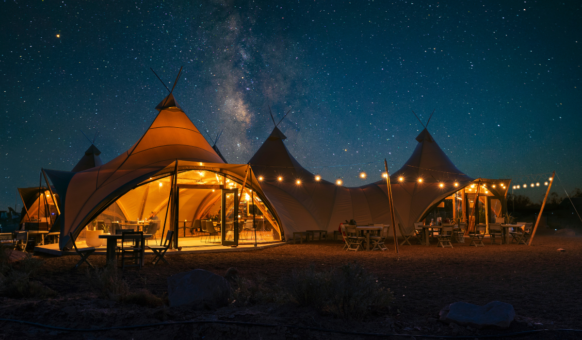 An illuminated large canvas tent sits beneath a star filled sky.
