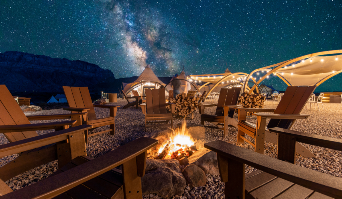 Chairs sit around a fire beneath a star filled night sky.