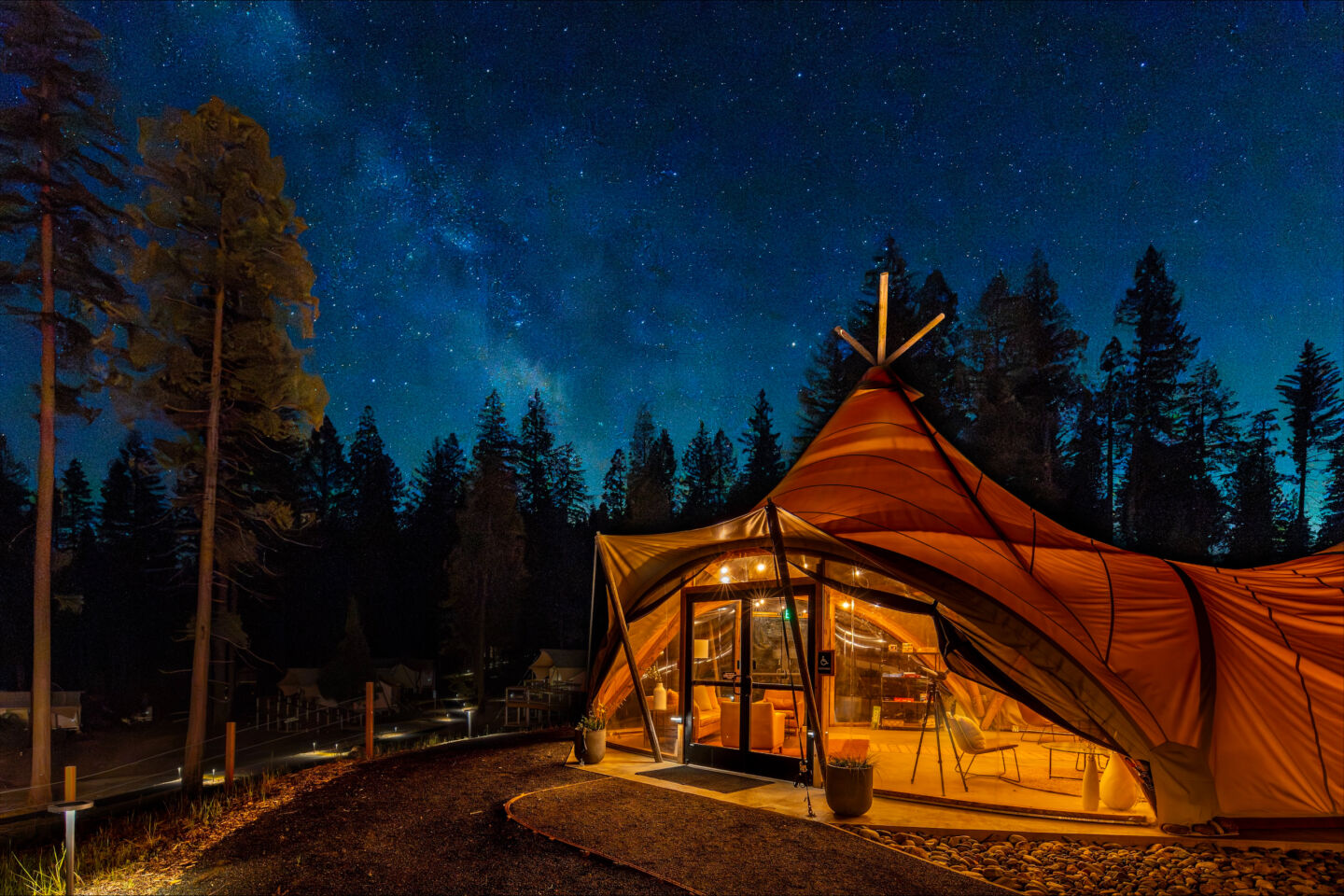 A large glamping ten under a star filled sky with a dark forest in the background.