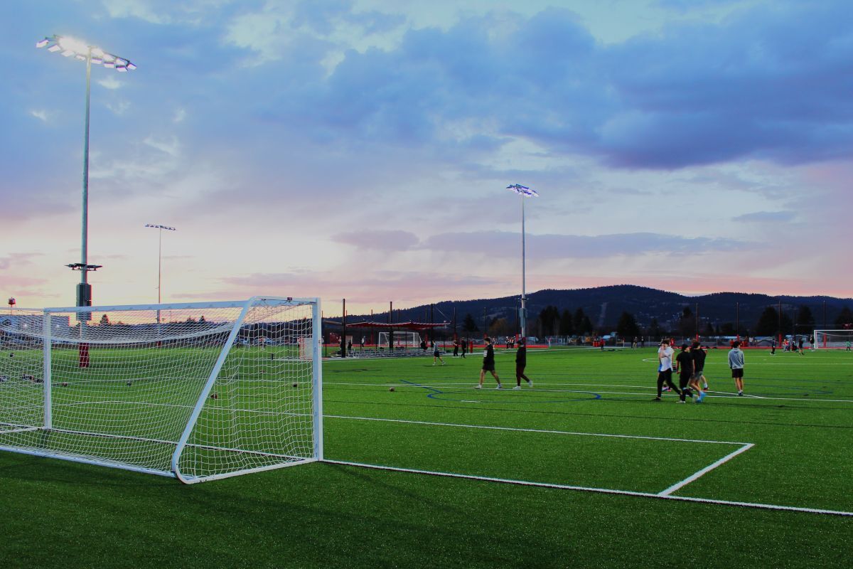 People play soccer at sunset on an illuminated field.