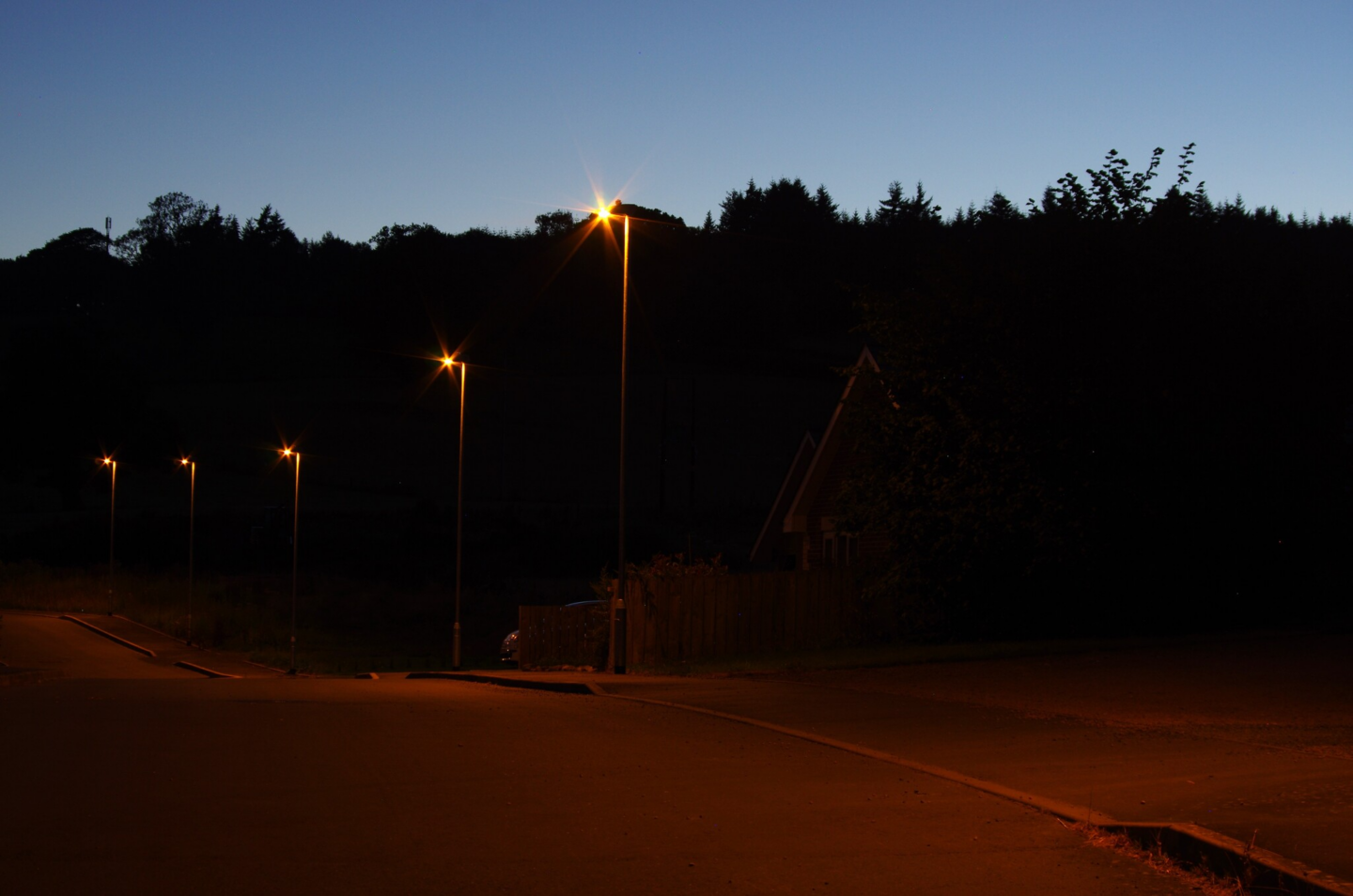 Photo of a street at night with lighting and woods behind