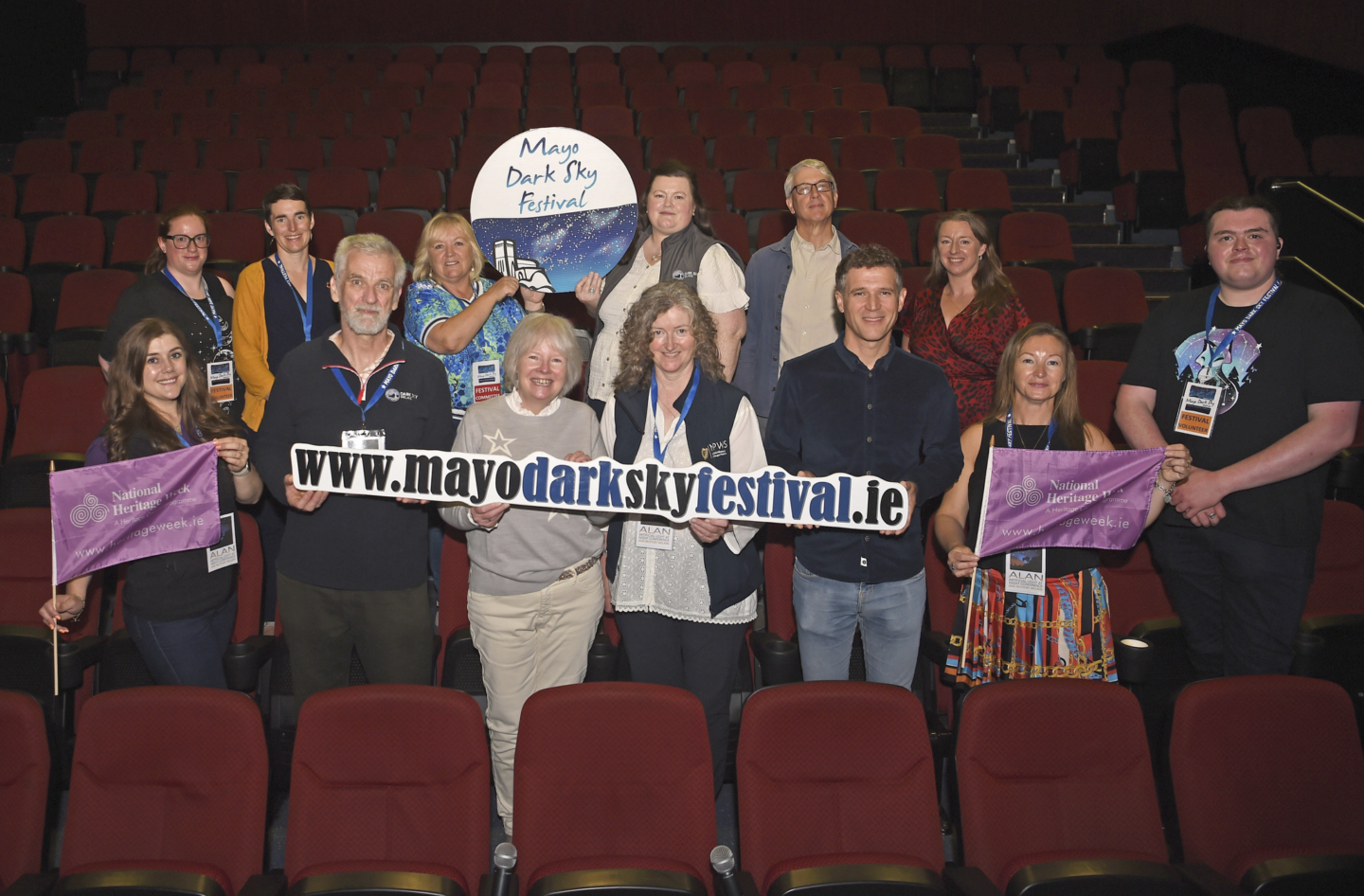 People stand in the audience section of a theater holding up a sign that says 