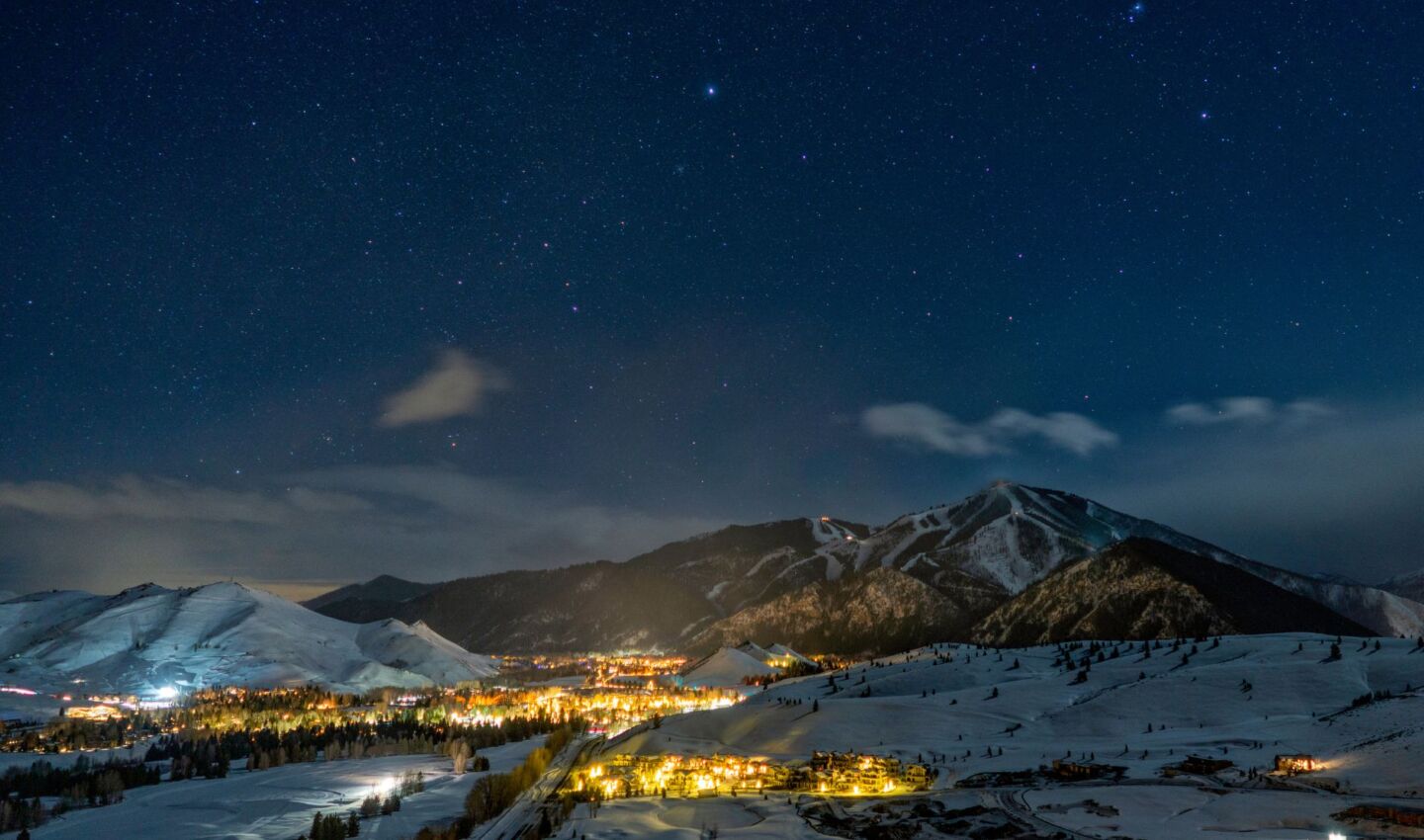 A snow-covered mountain valley glows beneath a clear, star-filled night sky. Warm lights from the resort village illuminate the landscape below, while ski runs trace the surrounding peaks and thousands of stars remain visible overhead, highlighting the contrast between responsible outdoor lighting and the natural darkness of the night sky.